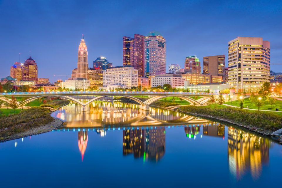 Twilight cityscape with illuminated buildings and reflective river.